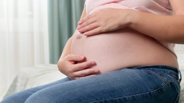Primo piano di bella donna incinta con grande pancia seduta sul letto e toccare il suo addome con le mani - Filmati, video