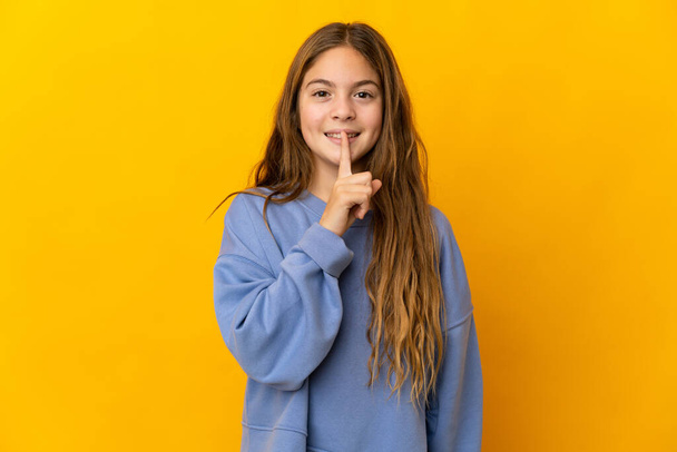 Child over isolated yellow background showing a sign of silence gesture putting finger in mouth - Foto, immagini