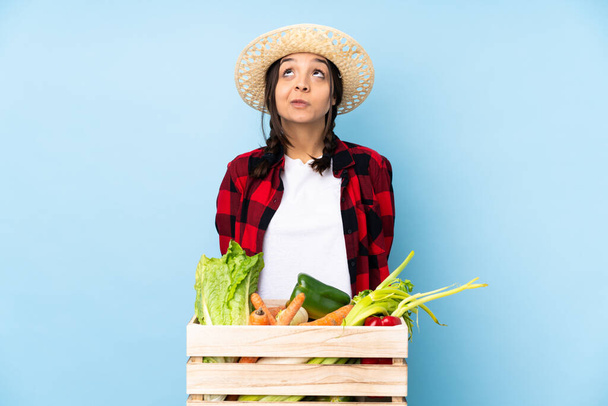 Mujer agricultora joven sosteniendo verduras frescas en una canasta de madera y mirando hacia arriba - Foto, imagen