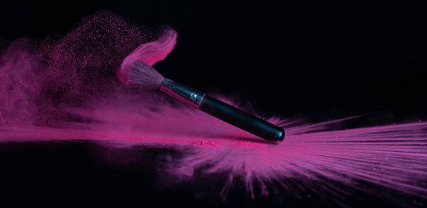Pink makeup powder brush fall on a shiny black surface in a dust cloud - Фото, изображение