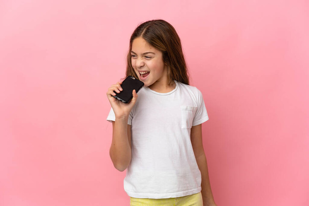 Παιδί πάνω από απομονωμένο ροζ φόντο χρησιμοποιώντας το κινητό τηλέφωνο και το τραγούδι - Φωτογραφία, εικόνα