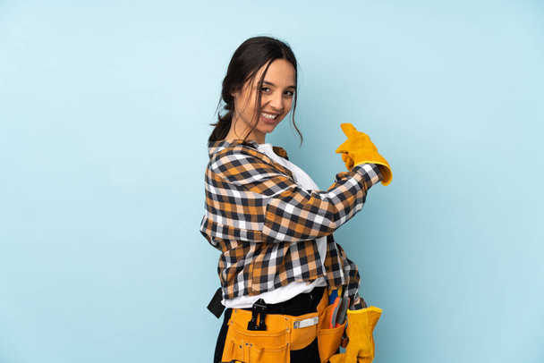 Young electrician woman isolated on blue background pointing back - Photo, Image