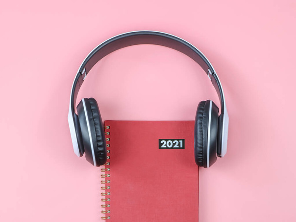 Widok z góry lub płaska leżanka z czerwonego pamiętnika 2021 lub planera pokrytego słuchawkami na różowym tle z miejscem do kopiowania. czego słuchać w 2021 r.. - Zdjęcie, obraz