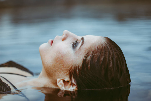 A nő a kádban, akinek csak az arca van a víz felett, egy gyönyörű nyugodt kifejezés. - Fotó, kép