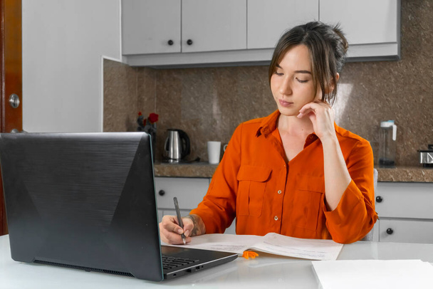 A young mixed race woman is sitting in the kitchen at home, chatting on a video call. Online work or home schooling concept. High quality photo - Photo, Image