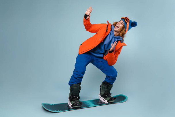 Young guy posing on a snowboard isolated over blue background - Photo, image