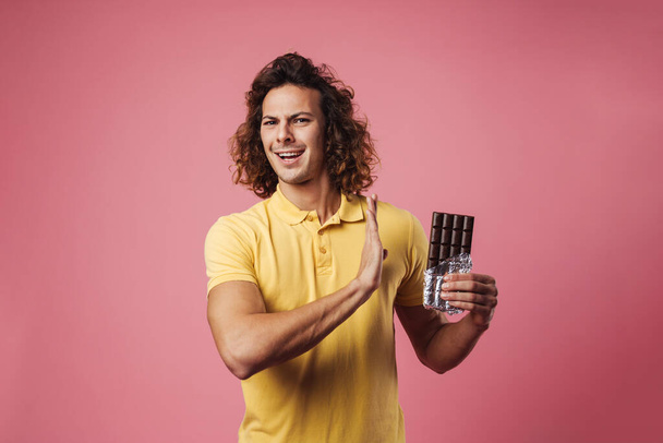 Serious man refusing eating chocolate isolated over pink background, stop gesture - Zdjęcie, obraz