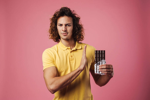 Serious man refusing eating chocolate isolated over pink background, stop gesture - Fotó, kép