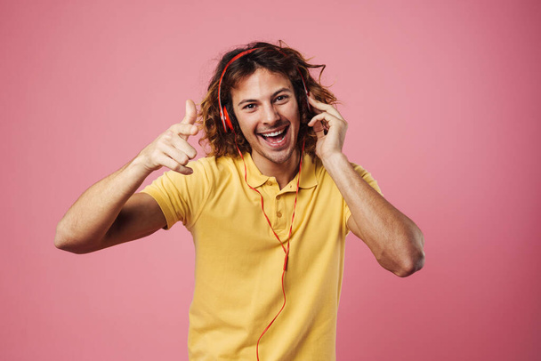 Happy guy listening music with headphones and pointing finger at camera isolated over pink background - Foto, immagini
