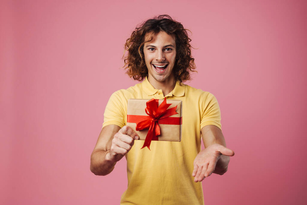 Happy handsome guy showing gift box and copyspace isolated over pink background - Фото, зображення