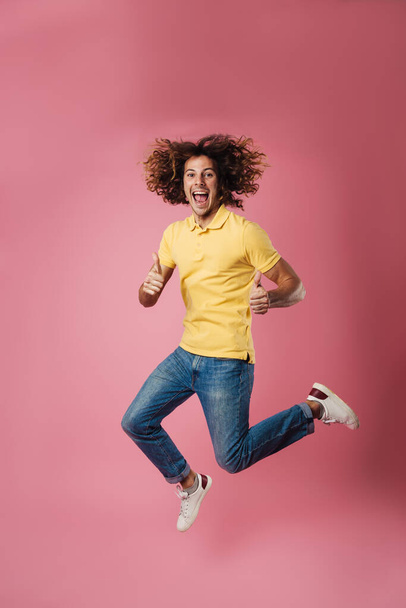 Excited handsome guy showing thumbs up while jumping isolated over pink background - Zdjęcie, obraz