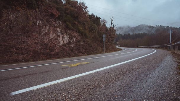 Islak, boş asfalt yol, yağmurlu, sisli bir kış sahnesinde dağ yoluna döner. - Fotoğraf, Görsel