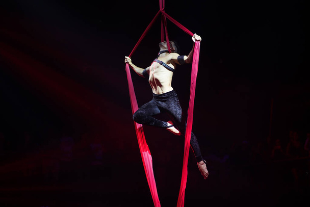 Brezilyalı güçlü seksi adam kırmızı ışıklarda hava ipekleriyle performans sergiliyor. Spor salonu ve yaşam tarzı konsepti. - Fotoğraf, Görsel