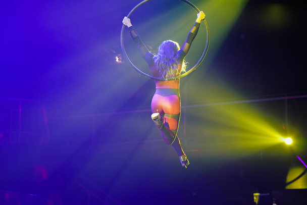 Flexible sexy athletische Frau, luftakrobatische Hoop-Performance, Frauen halten sich an lufthohen Reifen mit High Heels, die in gelbem Licht hinterleuchtet sind, Air Circus Show - Foto, Bild