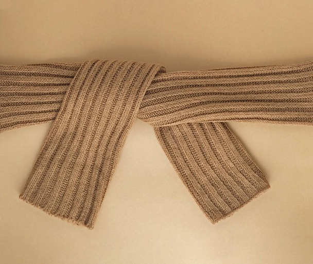 Hand knitted beige scarf on the pastel colored background. Knitted scarf tied in knot. Brown knitted scarf or sweater texture. Texture of warm crocheted clothing textile. Creative idea. Cozy concept.  - Photo, Image