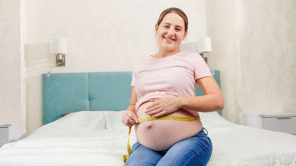 Беременная женщина ждет ребенка с помощью измерительной ленты, чтобы проверить ее размер и параметры тела. Концепция беременной медицины и здорового питания - Фото, изображение