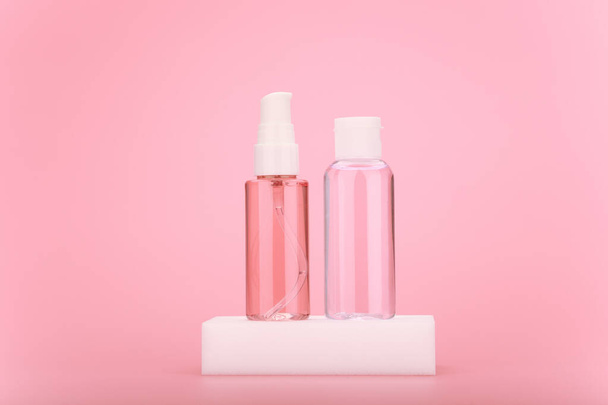 Cleaning foam or gel and moisturizing skin lotion in transparent bottle on white podium against bright pink background - Фото, изображение