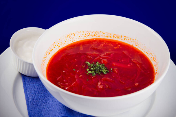Tazón blanco de sopa tradicional ucraniana y rusa sopa de remolacha o sopa de remolacha vegetal con crema agria sobre fondo azul. - Foto, Imagen