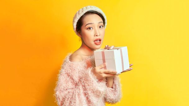 Image of a beautiful happy young asian woman posing isolated over yellow wall background holding present gift box. - Fotoğraf, Görsel