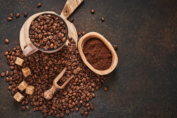 Coffee roasted beans in cup and scattered nearby, ground coffee and cane sugar on a brown table background. Top view with space to copy text. - Fotoğraf, Görsel