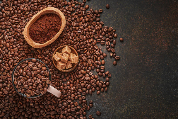 Coffee roasted beans in cup and scattered nearby, ground coffee and cane sugar on a brown table background. Top view with space to copy text. - Φωτογραφία, εικόνα