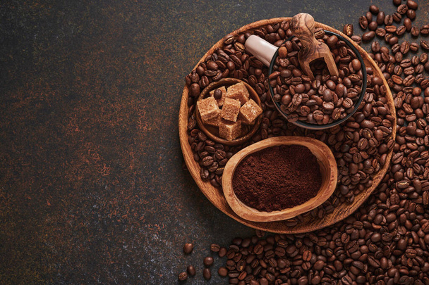 Coffee roasted beans in cup and scattered nearby, ground coffee and cane sugar on a brown table background. Top view with space to copy text. - Фото, изображение