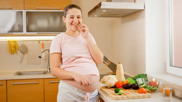 Retrato de mujer embarazada feliz sonriente cocinando en la cocina y esperando verduras frescas y sabrosas. Concepto de estilo de vida saludable y nutrición durante el embarazo - Foto, imagen