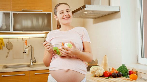 Happy smiling pregnant woman with big belly holding big bowl with fresh vegetable salad - Fotoğraf, Görsel
