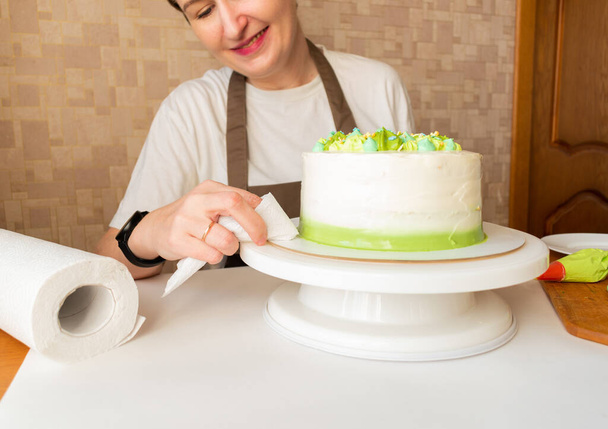 緑のホイップクリームを入れて、自宅でお誕生日ケーキを飾るために菓子袋を使用して女性。自家製料理のコンセプトとケーキを飾る。菓子作りの女性. - 写真・画像