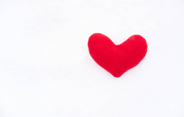 Small red soft toy heart lies on white snow. Valentines day greeting card and lot of empty space for your greeting text. - Photo, Image