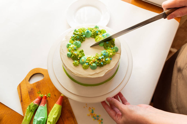 Woman in apron is cut off fresh baked Birthday cake. Homemade cake for Birthday celebration. Home baking concept. Isolated. Copy space. Leisure and hobby. - 写真・画像