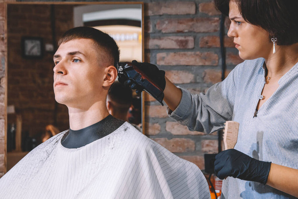 Krásná žena kadeřnice holí klientovi hlavu elektrickým trimrem v holičství. Koncept reklam a holičství. - Fotografie, Obrázek