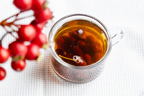 Fruit tea made from berries and rosehip fruits in a transparent glass mug. Hot drink like fresh compote on a white towel - Φωτογραφία, εικόνα