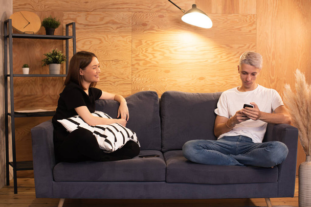Young happy couple sitting on the couch. Man is sitting on the phone - Photo, Image