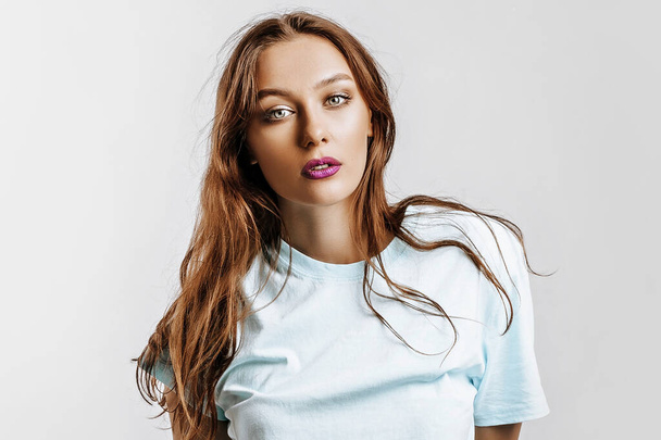 Beautiful young brunette girl with green eyes with long hair with fashion makeup with purple lips on an isolated gray background. The woman seriously looking at the camera. Kind cute model - Φωτογραφία, εικόνα
