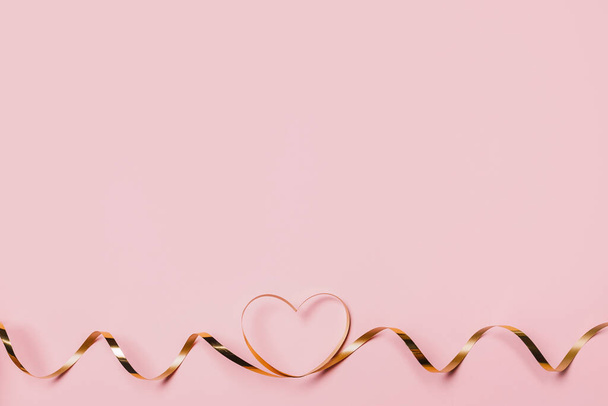 shape heart by gold ribbon on isolated pink background - Fotó, kép