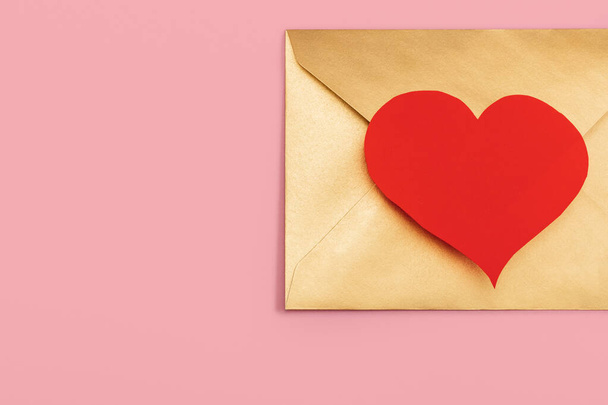 Sobre de papel dorado con corazón rojo aislado sobre fondo rosa - Foto, imagen