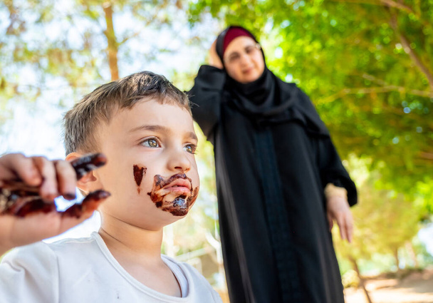 Η αραβίδα μητέρα θυμώνει με το γιο της γιατί τον σκέπασε με σοκολάτα. - Φωτογραφία, εικόνα