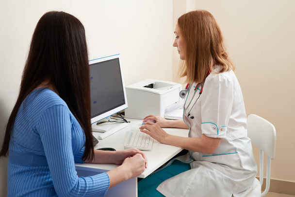 Doctora hablando con paciente joven sentada en un escritorio en el consultorio - Foto, Imagen