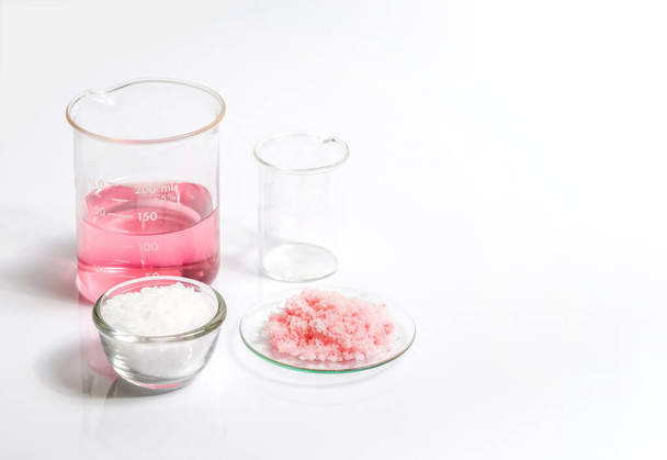 Chemicals for beauty care on white laboratory table. Pink flake chemicals in Chemical Watch Glass, Microcrystalline wax in glass container. - Photo, Image