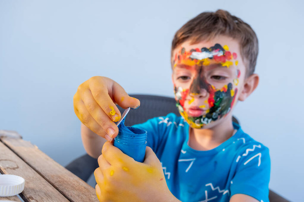 Το αγόρι παίζει με τα χρώματα χρησιμοποιώντας τα χέρια του και το πρόσωπό του - Φωτογραφία, εικόνα