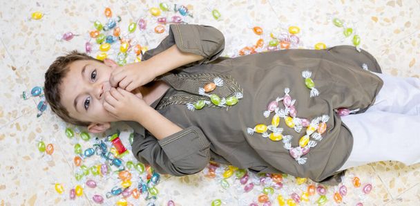 Boy laying on the ground surrounded by candy - Φωτογραφία, εικόνα