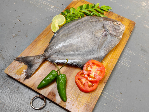 Lähikuva näkymä Tuore musta Pomfret kala koristeltu yrttejä ja vihanneksia, Valikoiva keskittyä. - Valokuva, kuva