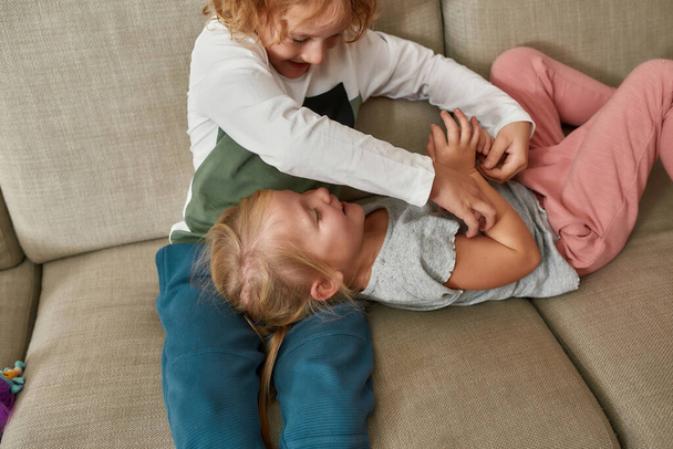 Adorable boy tickling his little sister while playing together, cuddling on a sofa at home - Photo, image