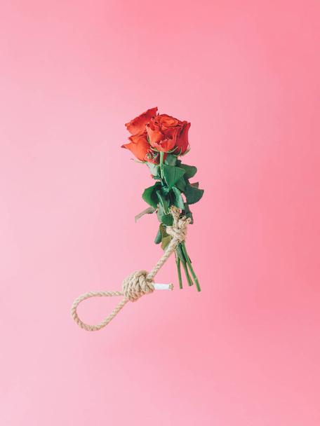 Creative Valentines composition with rose bouquet and hangmans noose against pastel pink background. - Fotó, kép