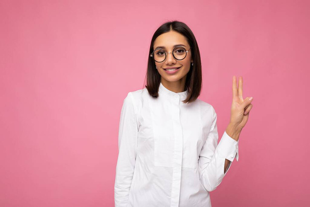 Attractive happy smiling young brunette woman wearing everyday stylish clothes and modern optical glasses isolated on colorful background wall looking at camera and showing three fingers - Photo, Image
