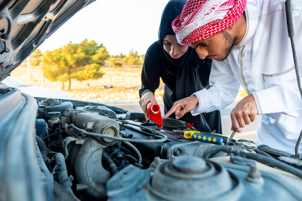 Arabische vrouw en haar man gieten olie in de motor van de auto - Foto, afbeelding