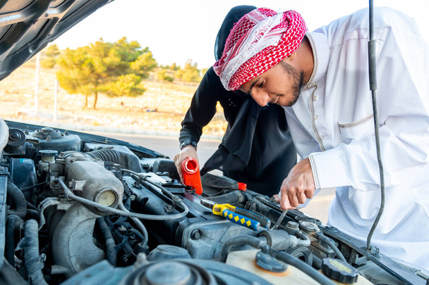 Arabische Frau und ihr Mann gießen Öl in den Automotor - Foto, Bild
