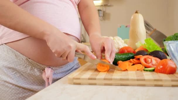 Primer plano de la mujer embarazada con el vientre grande cortar las verduras y la sal de cocina en la cocina. - Metraje, vídeo