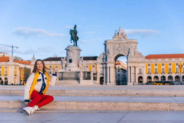 стильная девушка, сидящая на лестнице на фоне памятника королю Иосифу I и триумфальной арки. Лиссабон.  - Фото, изображение